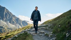 Randonneuse adulte portant une veste coupe vent unie sur sentier de montagne sans logo ni texte