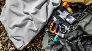 petit kit de réparation randonnée disposé sur sac outdoor et tissu neutre, sans texte ni logo